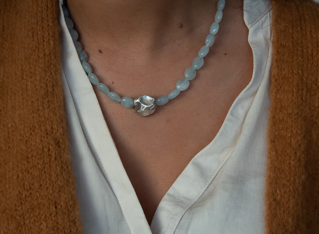 Collier de perles bleu clair et pièce centrale argentée, porté